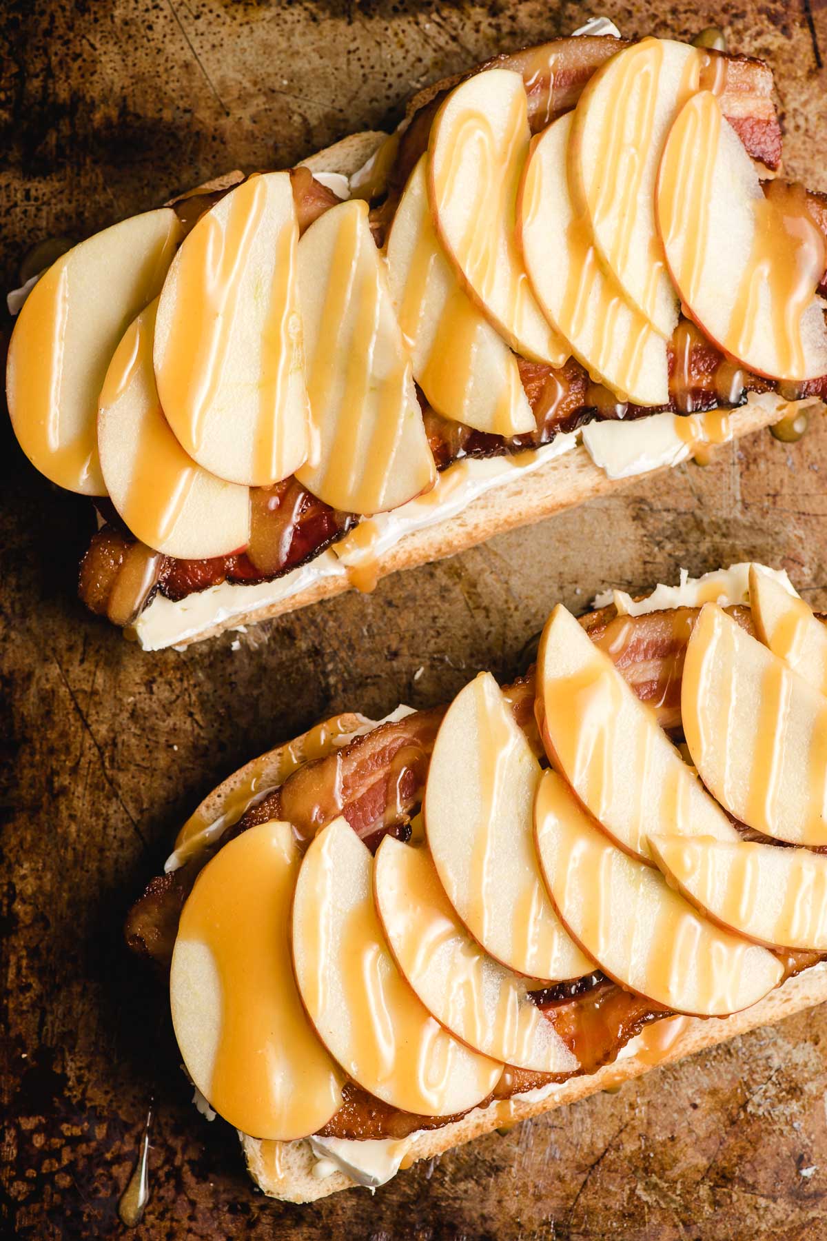 Two slices of bread topped with brie cheese, bacon, apple slices, and a drizzle of honey mustard.