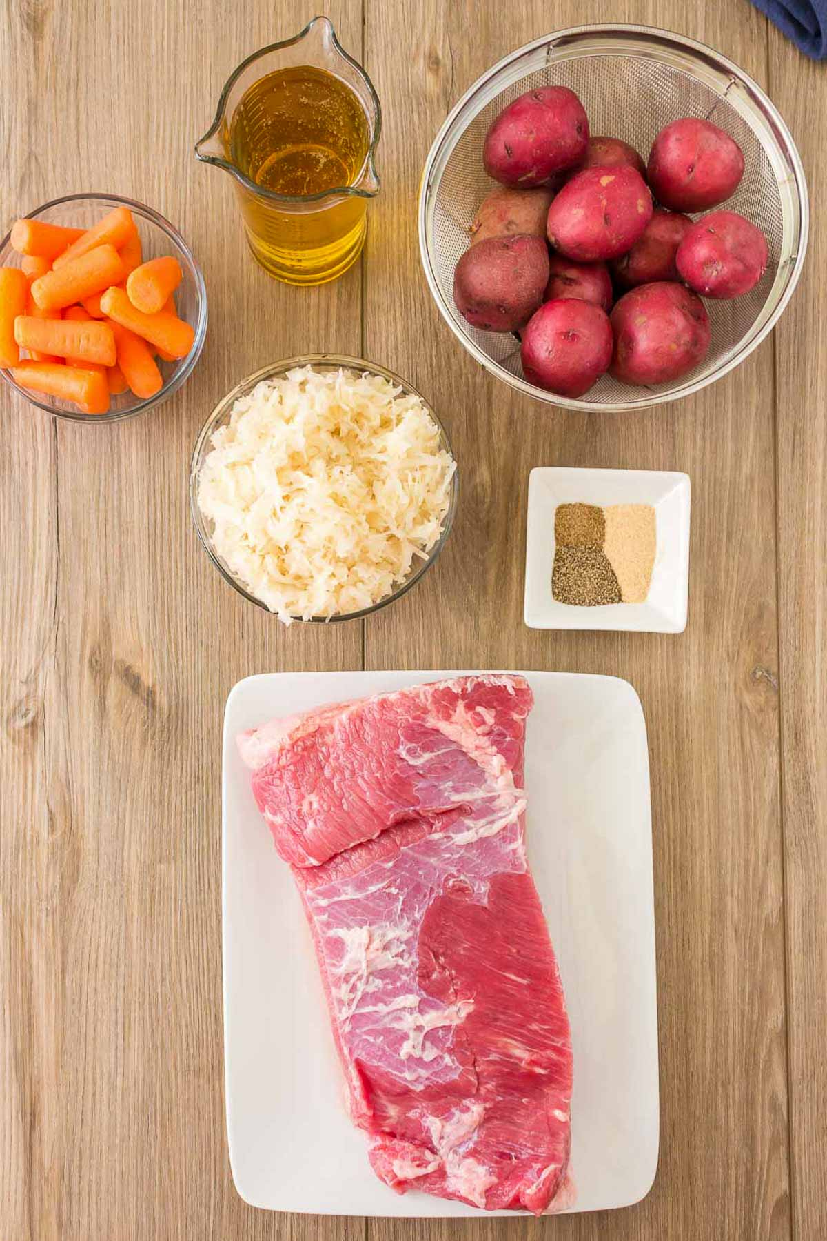 Ingredients for a corned beef recipe in bowls- corned beef brisket, sauerkraut, carrots, potatoes, beer, and seasonings.