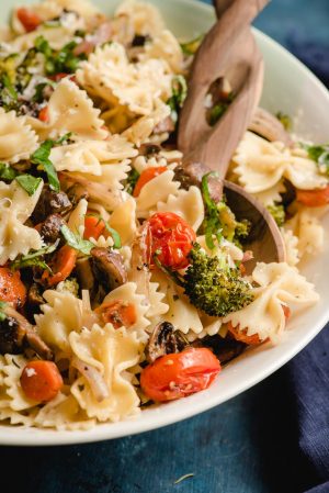 Wooden spoon scooping Roasted Veggie Pasta out of a large bowl.