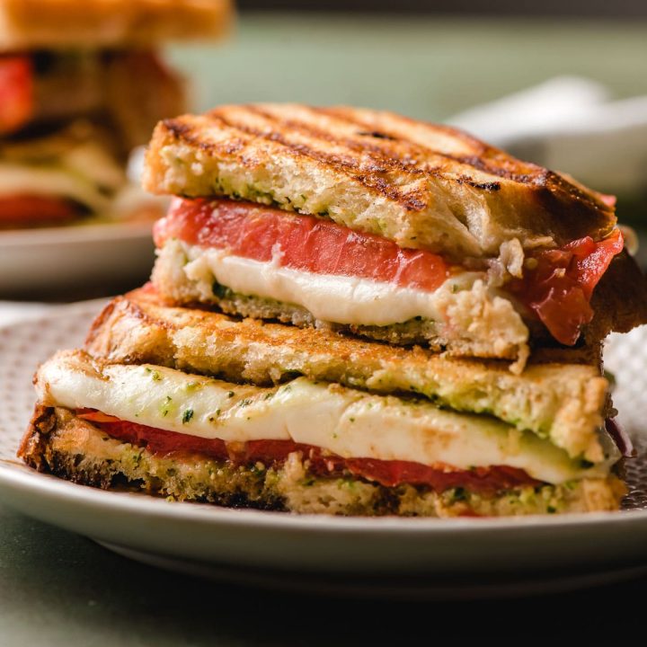 Caprese Panini halved and stacked on a white plate, with mozzarella melting down the front.