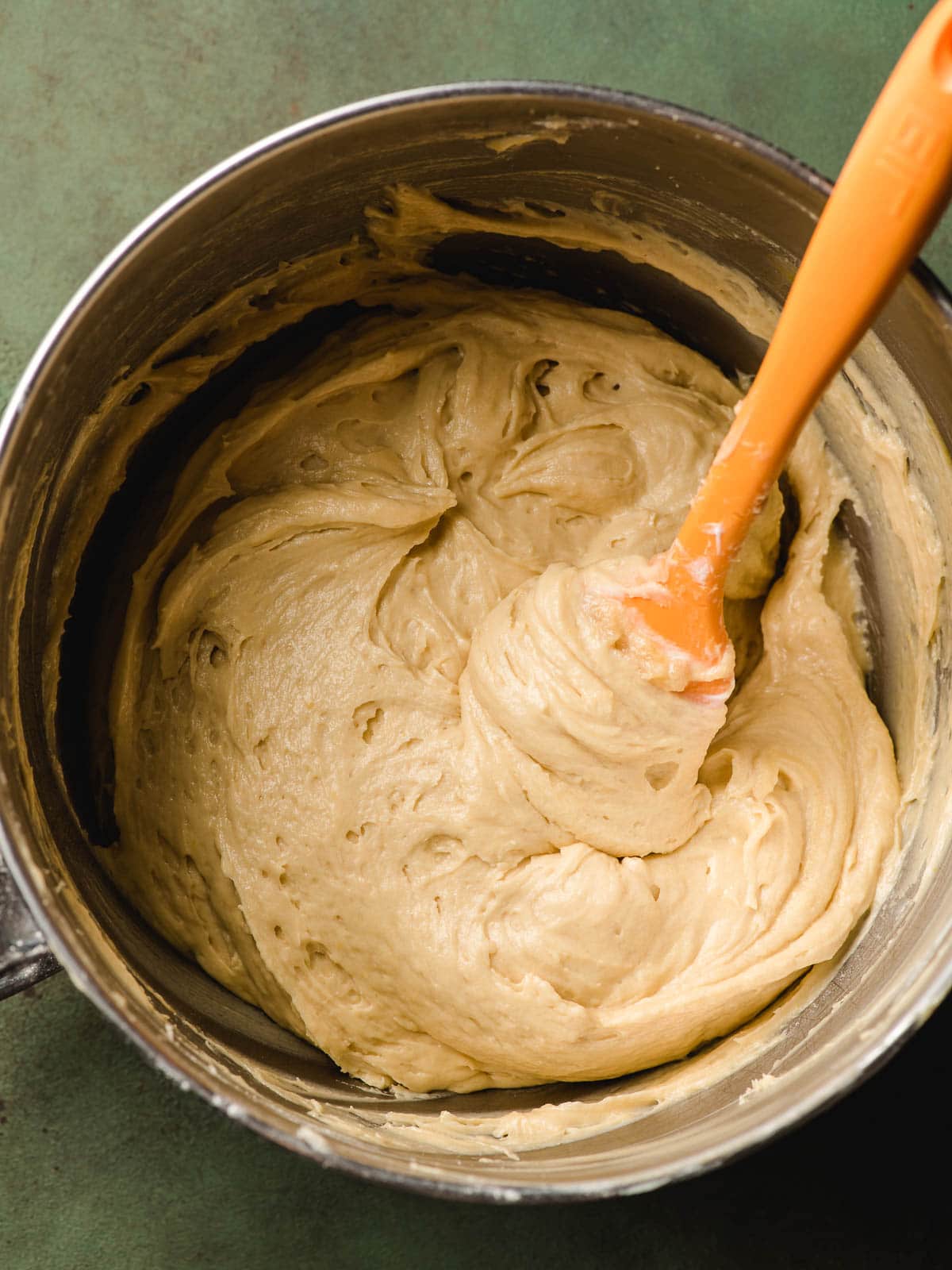 Bundt cake batter in a mixing bowl with an orange spatula.