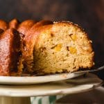 Slice of peach bundt cake being removed from a platter.