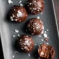 Gray rectangular plate with five double chocolate truffles on it. They've ben sprinkled with sea salt and one of them has a bite taken out of it.