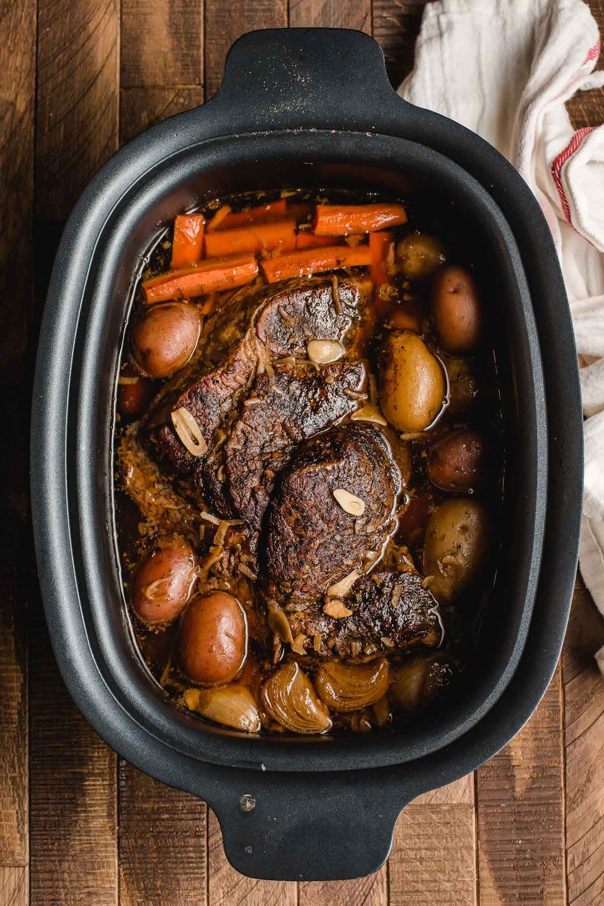 Slow cooked pot roast, potatoes, and carrots, shown in a crock pot.