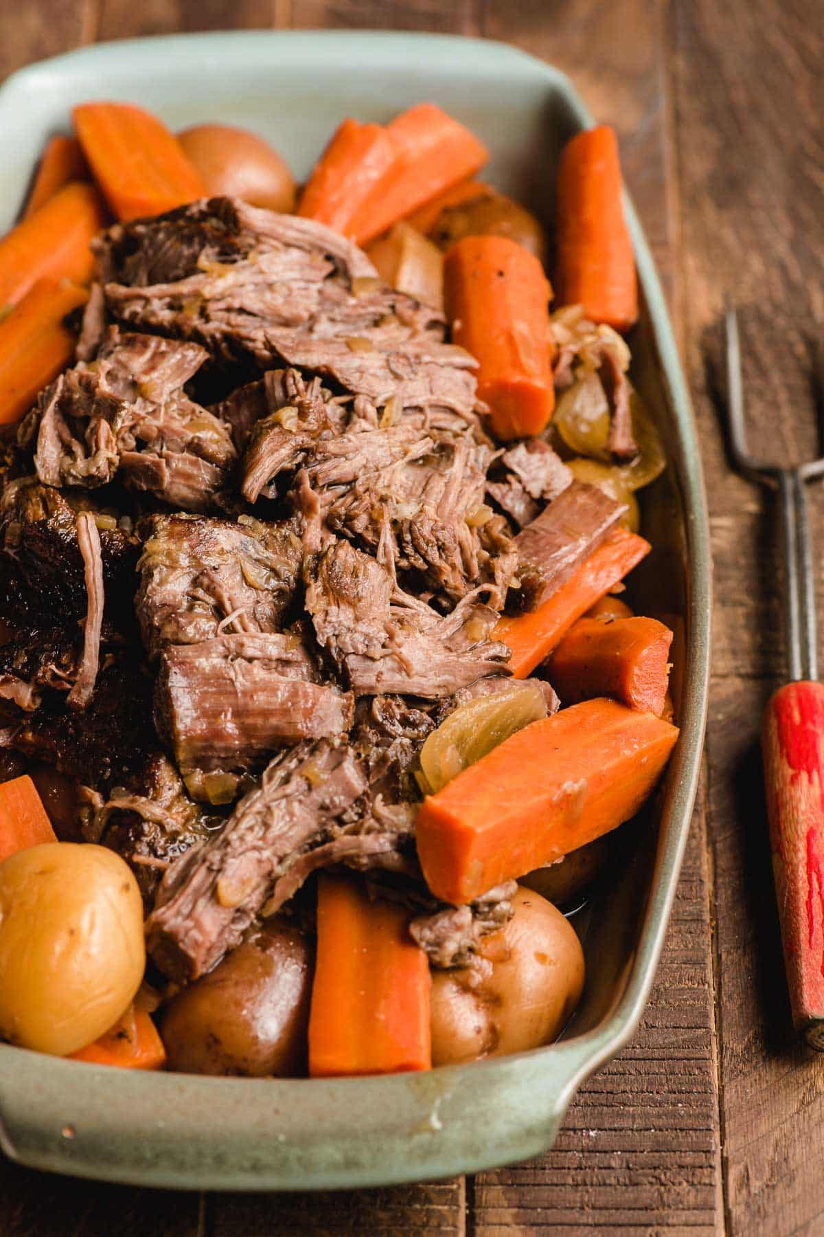 Tender pieces of pot roast piled on carrots and potatoes on a rectangular platter.