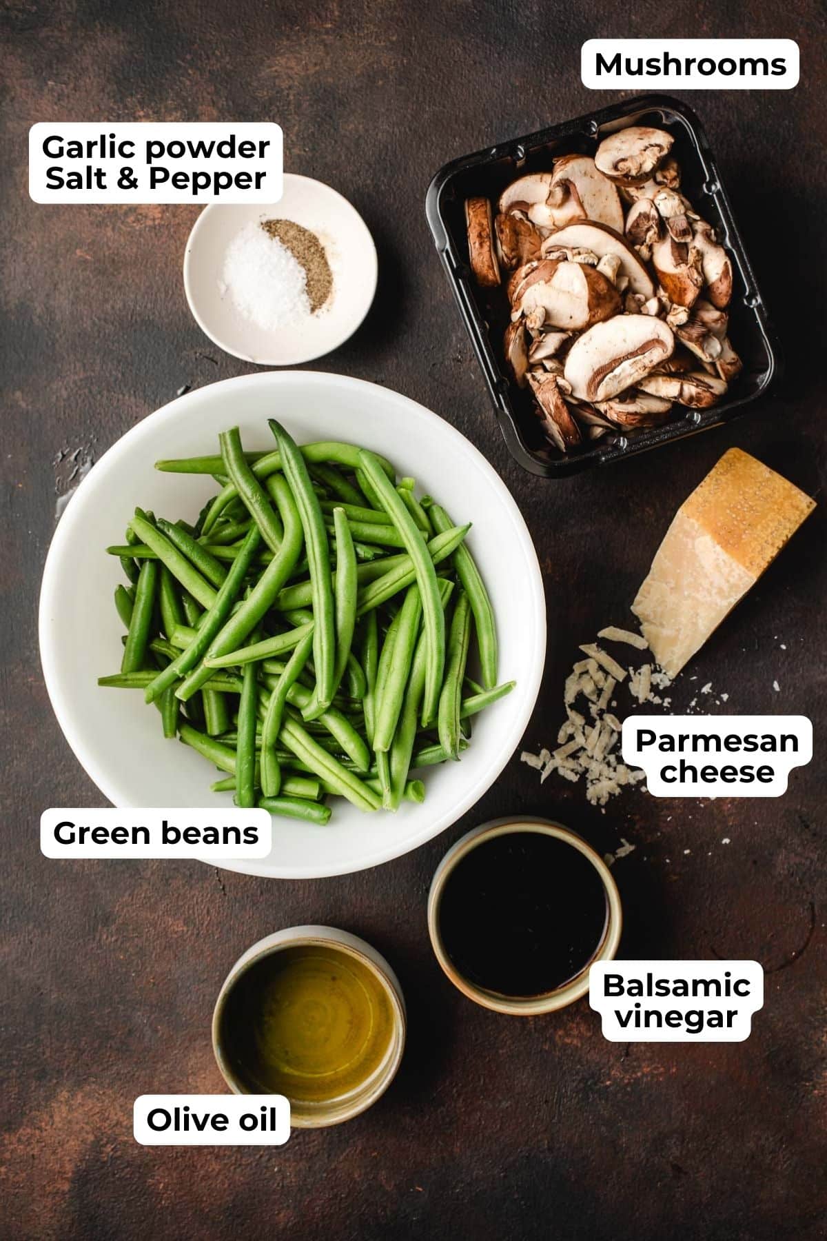 Bowl of green beans surrounded by bowls of salt and pepper, olive oil, balsamic vinegar, Parmesan cheese, and mushrooms.