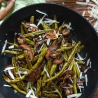Balsamic green beans on a plate with mushrooms and shredded parmesan cheese.