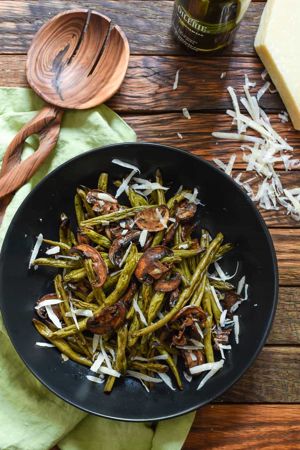 Roasted green beans and mushrooms on a blue plate with a serving spoon on the side.