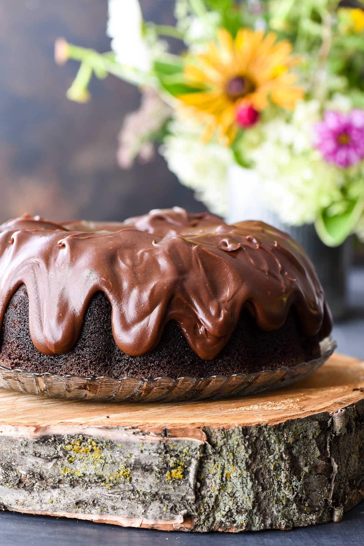 Chocolate Bundt Cake with Chocolate Frosting on a glass plate on top of a wood platter.