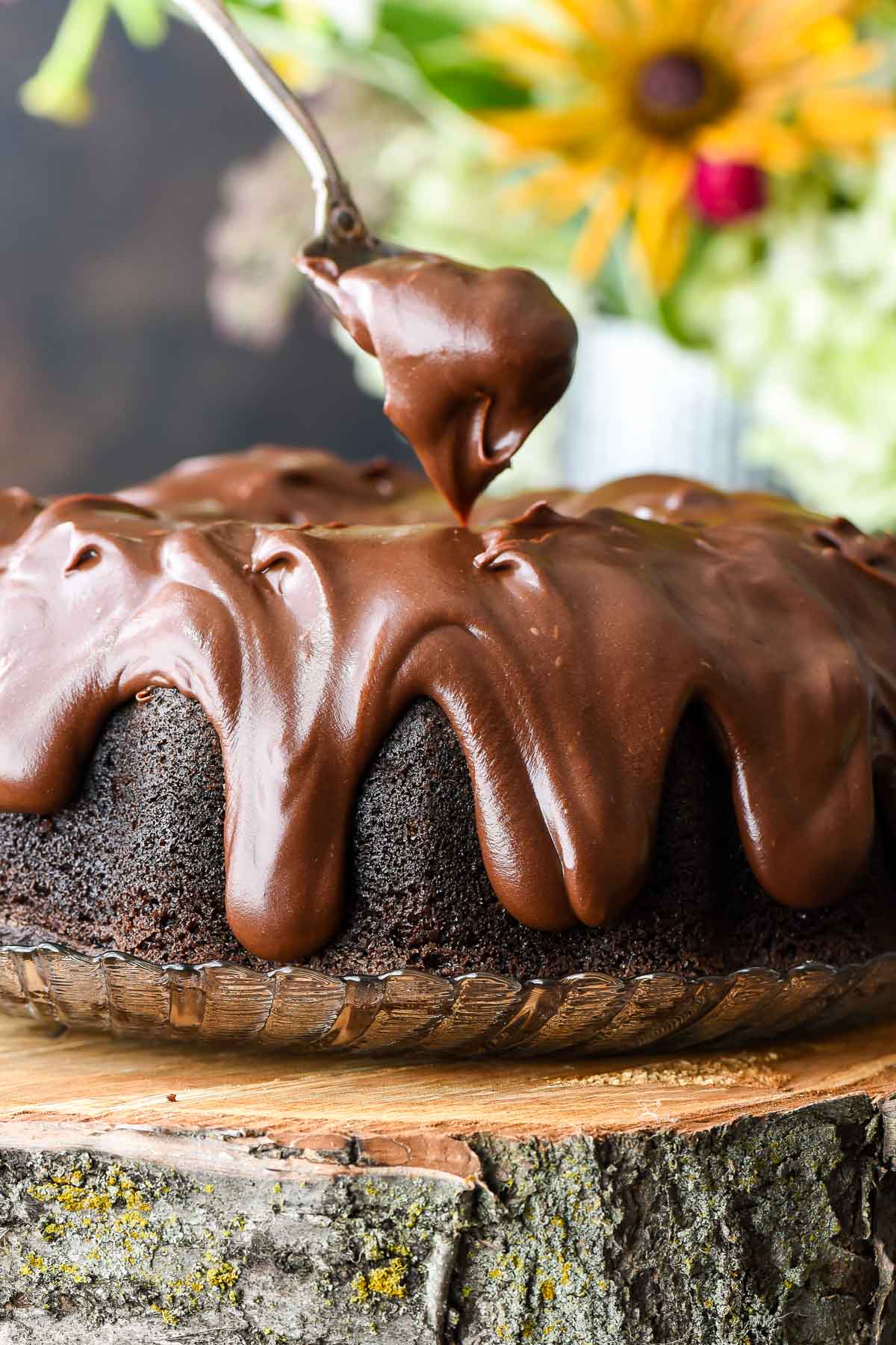 Spoon dolloping chocolate sour cream frosting onto a chocolate bundt cake.