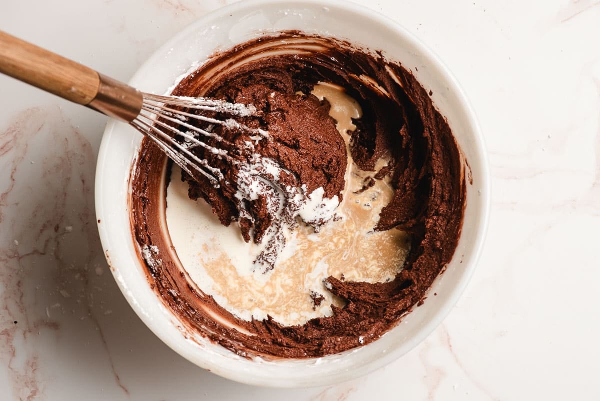 Cream and coffee whisked into chocolate frosting in a mixing bowl.