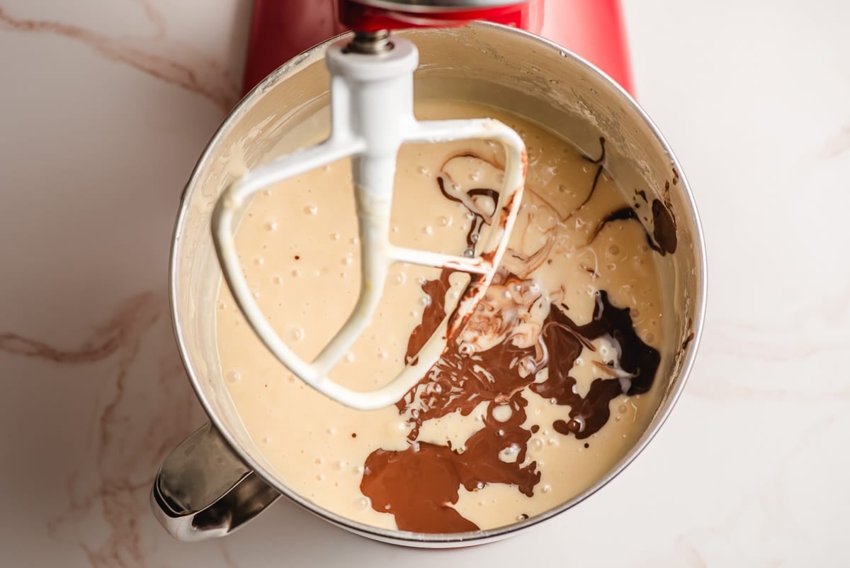 Coffee and cocoa mixture being stirred into cake batter in the bowl of an electric mixer.