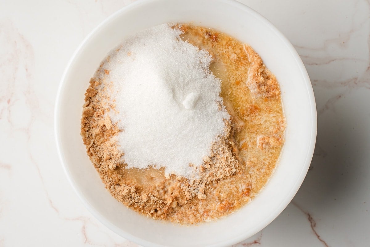 Graham cracker crumbs, melted butter, and granulated sugar in a white bowl.