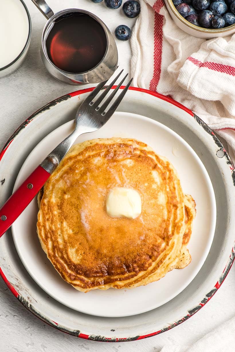 fluffy pancakes on a white plate with butter on top