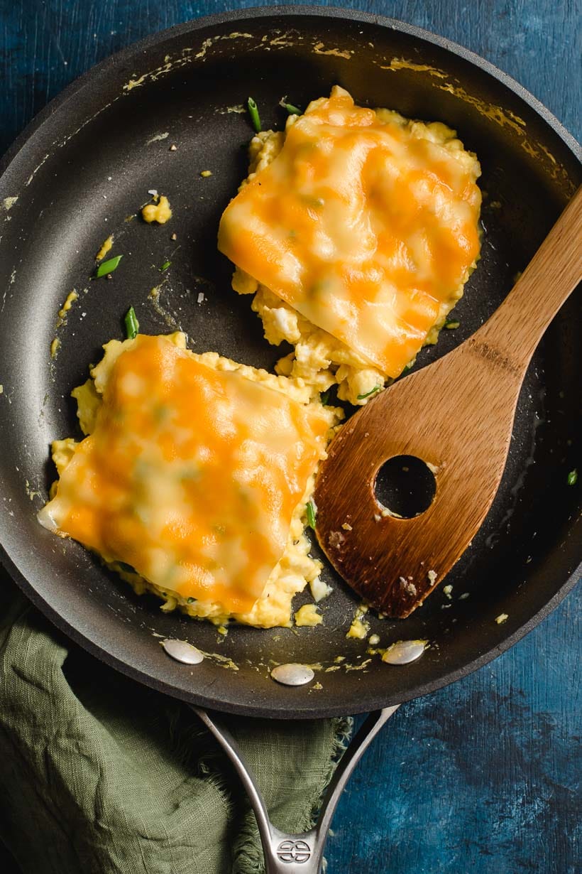 Two piles of scrambled eggs in a black skillet, both with a slice of melted cheese on top.