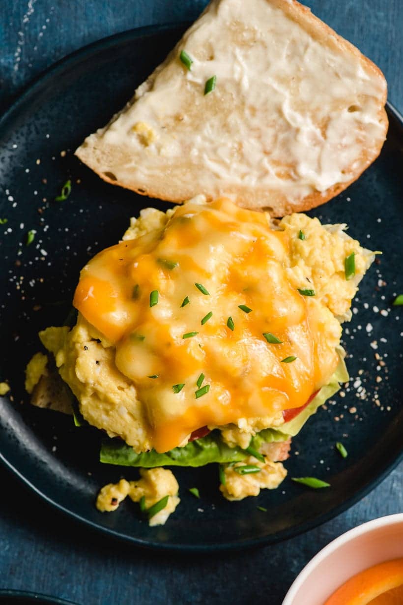 Scrambled eggs topped with melted cheese and green onions on a slice of bread.