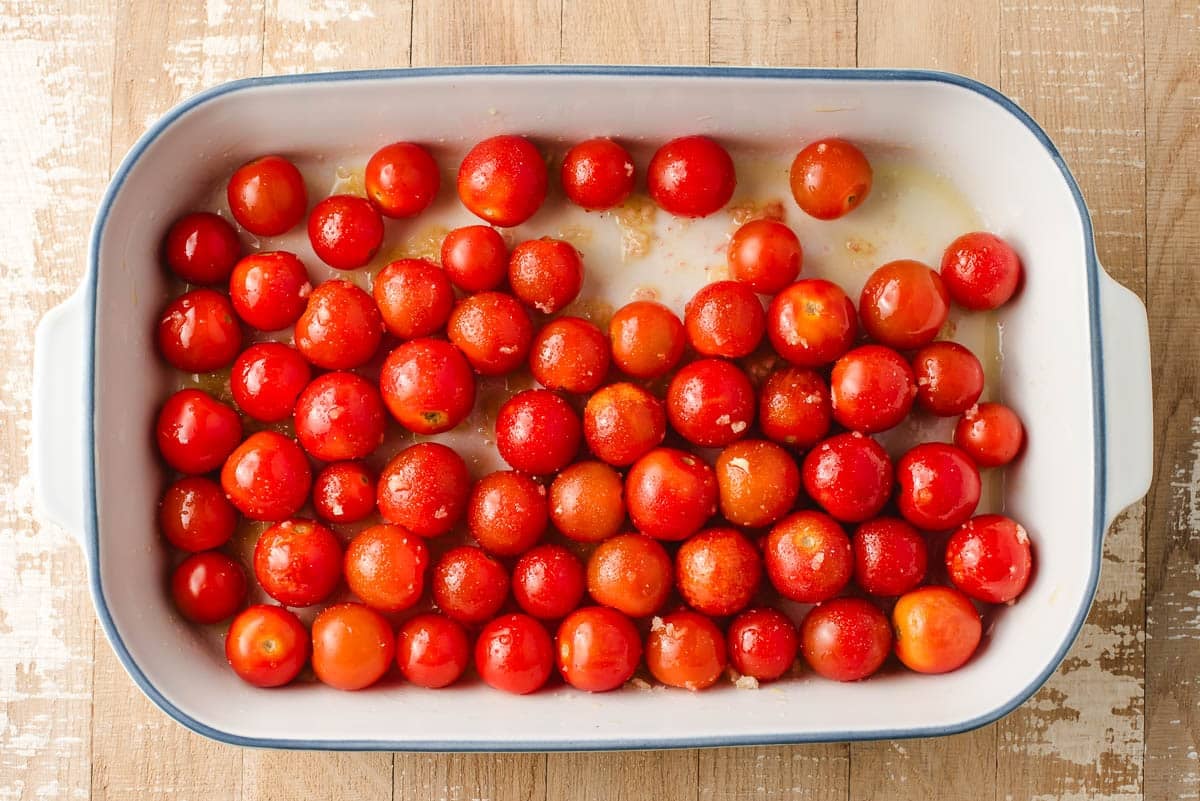Cherry tomatoes with garlic and olive oil in a baking dish.