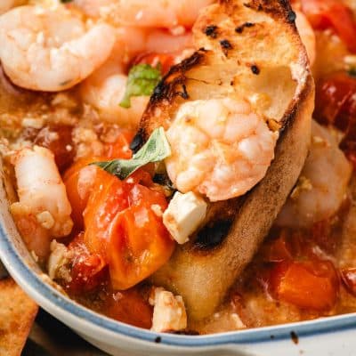 Toasted bread scooping up shrimp and roasted tomatoes.