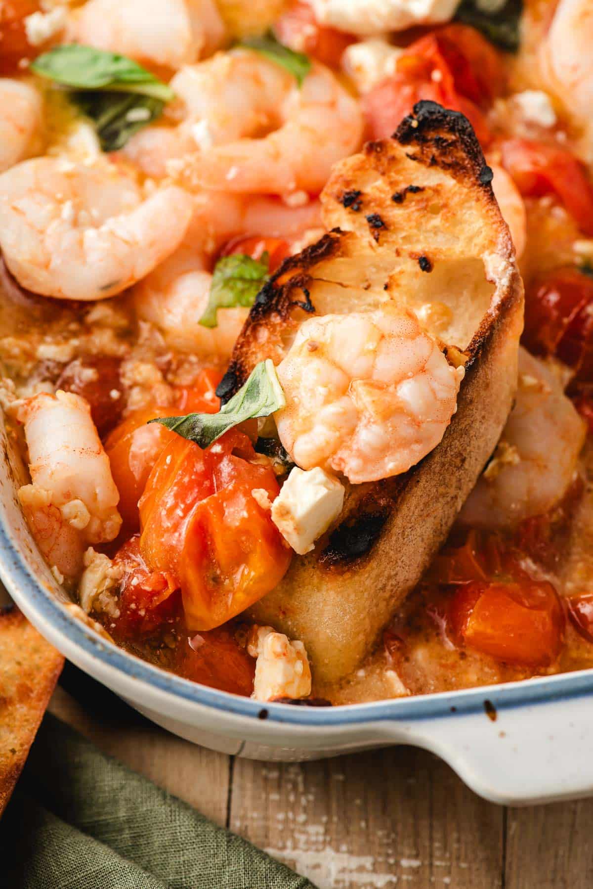 Toasted bread scooping up shrimp and roasted tomatoes.