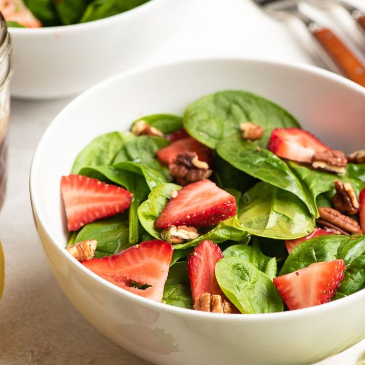 bowl of spinach salad with sliced strawberries and pecans