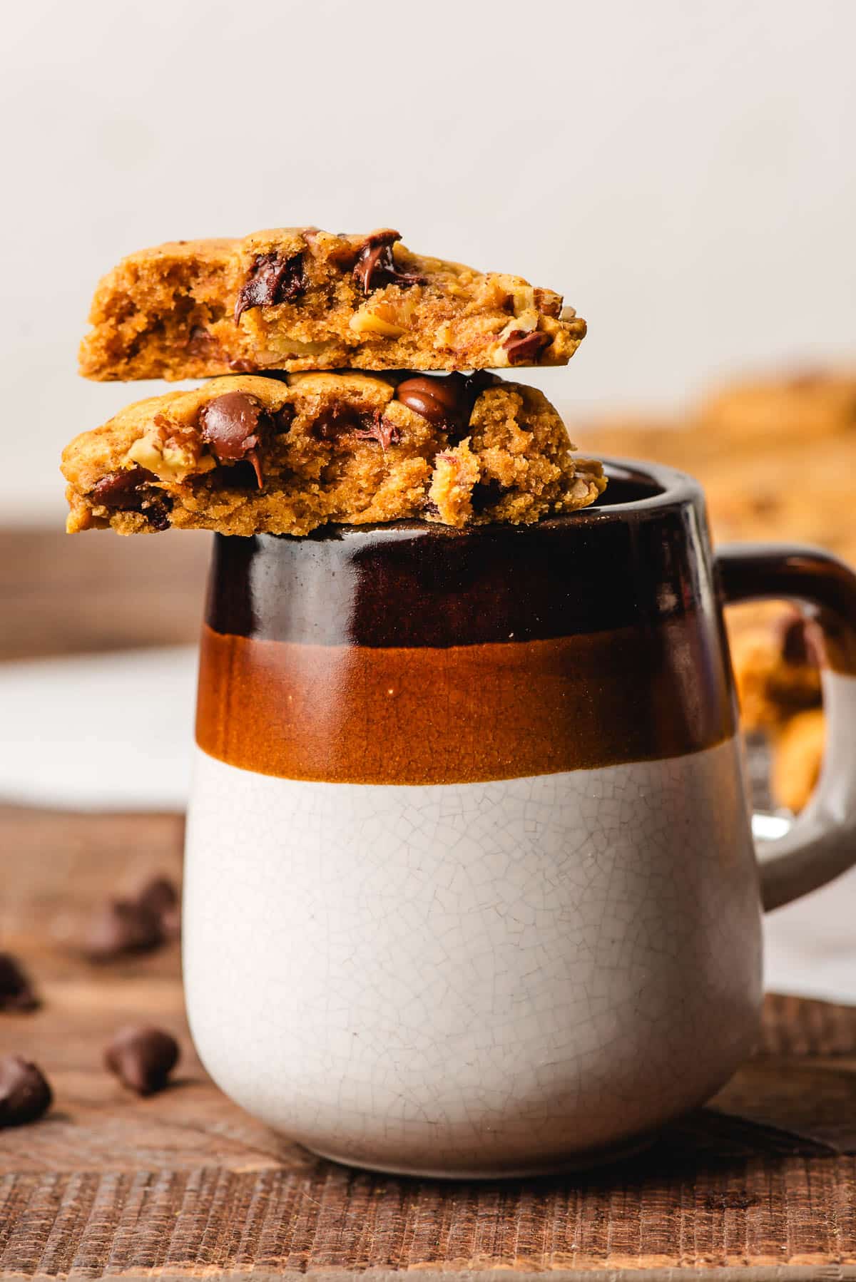 Halved pumpkin chocolate chip cookie stacked on a mug.