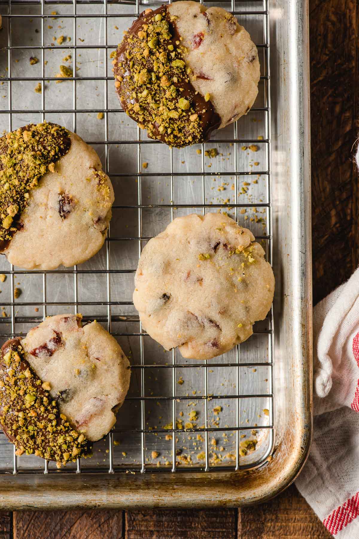 Chocolate and pistachio dipped shortbread cookies on a cooling rack on top of a baking sheet.