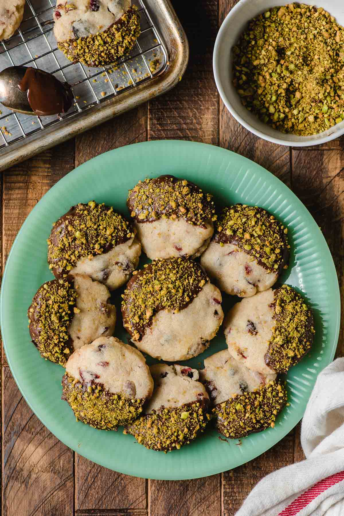 Chocolate dipped cranberry shortbread cookie sprinkled with pistachios and displayed on a green jadette plate.