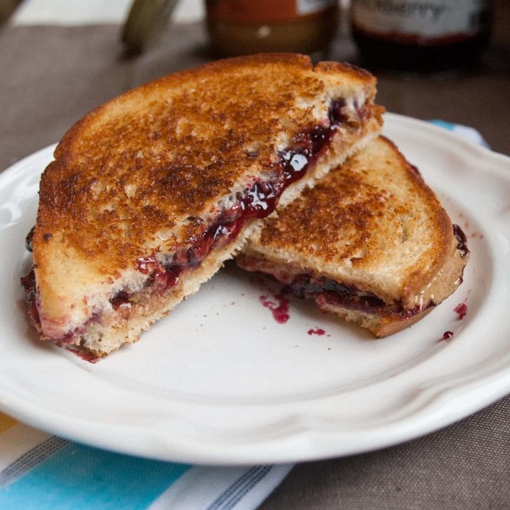 Grilled peanut butter and jelly sandwich, halved, and served on a white plate.