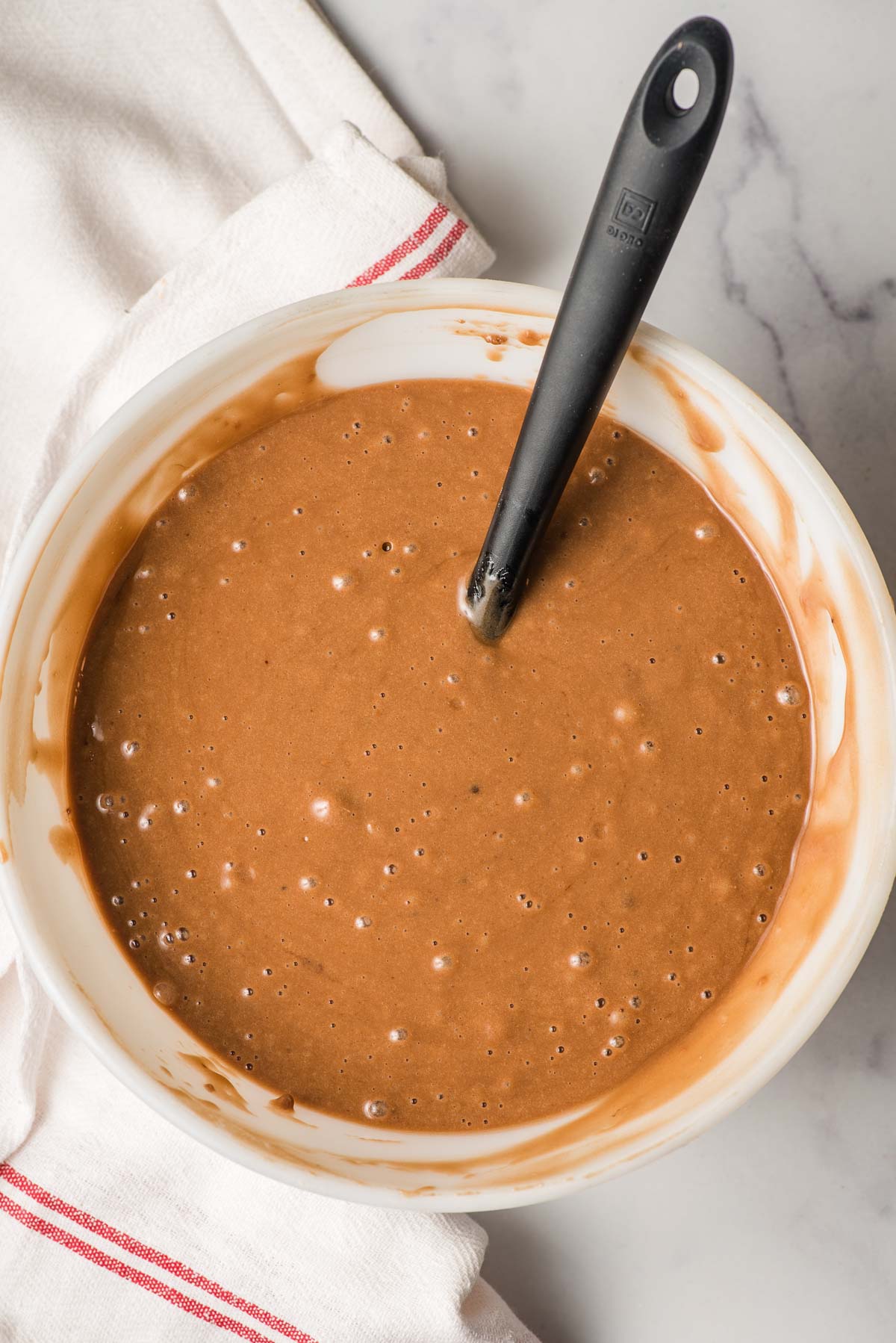 White mixing bowl with chocolate cake batter and a spatula.