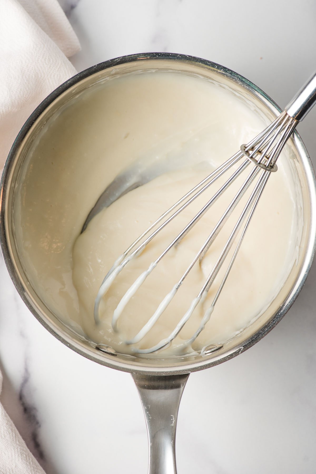 Whisk mixing together cooked flour and milk in a sauce pan.