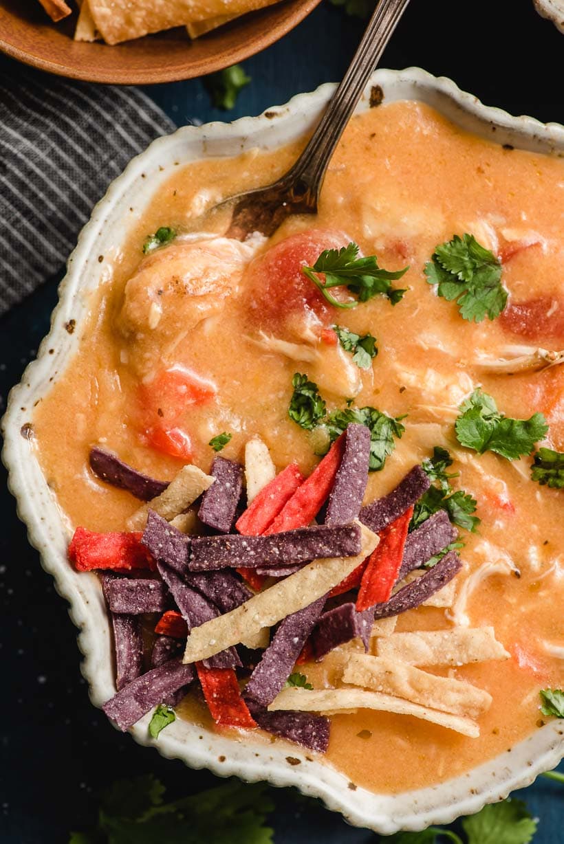 Scalloped bowl filled with spicy chicken tortilla soup and topped with cilantro and tortilla chips.