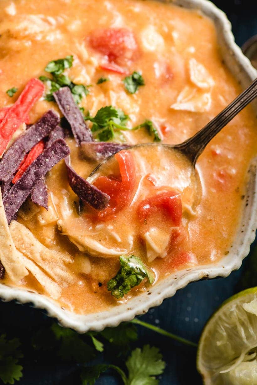 Bowl of tortilla soup with a spoon lifting a bite out.