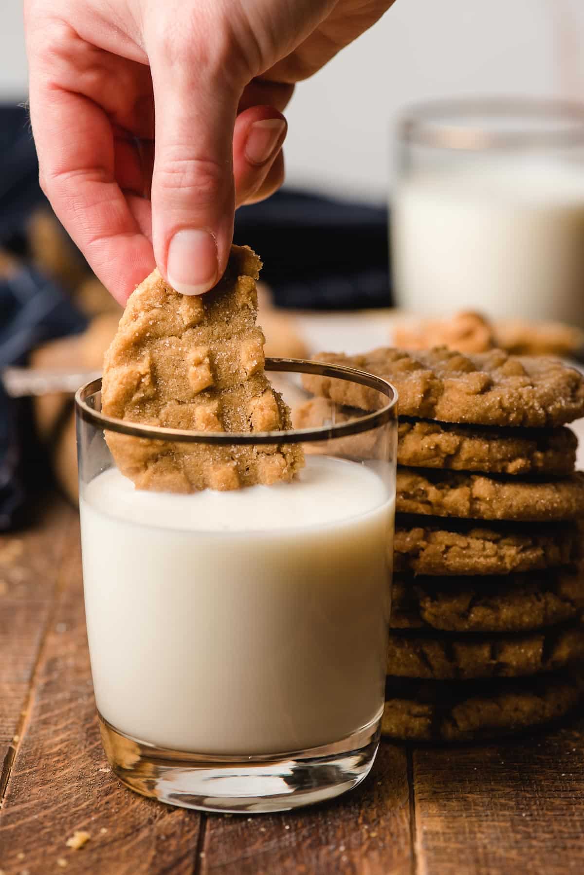 Hand dunking half of a peanut butter cookie into a glass of milk.