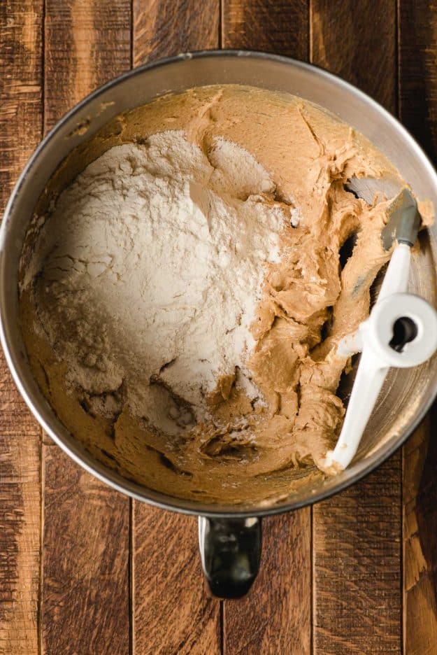 Flour added to a chewy peanut butter cookie dough base in a mixing bowl.