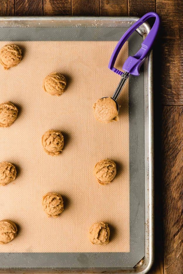 Tray of unbaked peanut butter cookies, with a cookie scoop holding one round of dough.