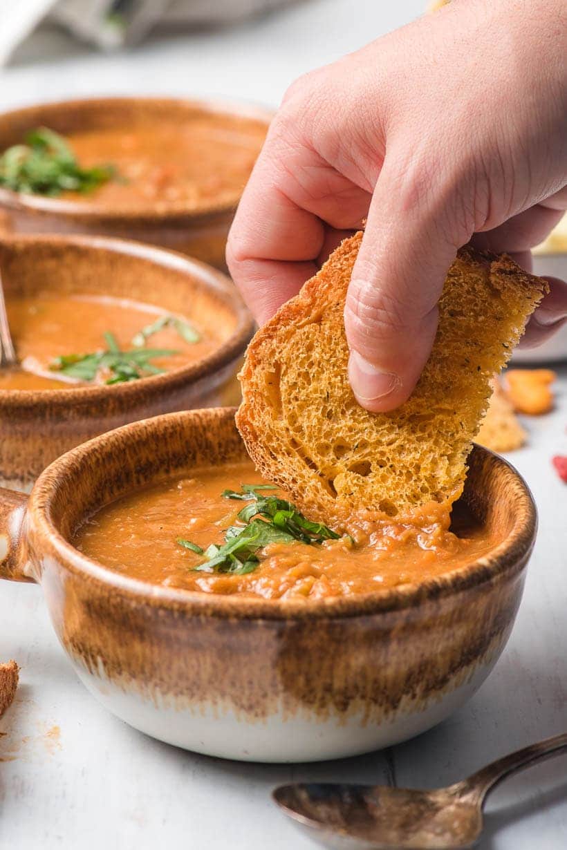 white hand dipping bread into a bowl of lentil stew