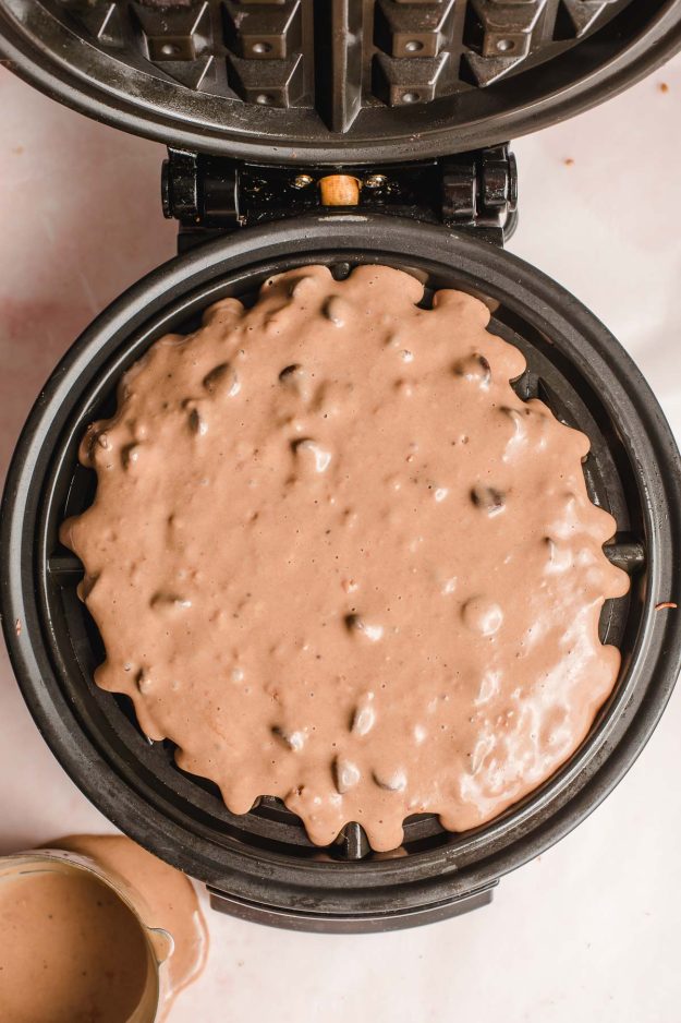 Chocolate chip waffle batter shown in a waffle iron.