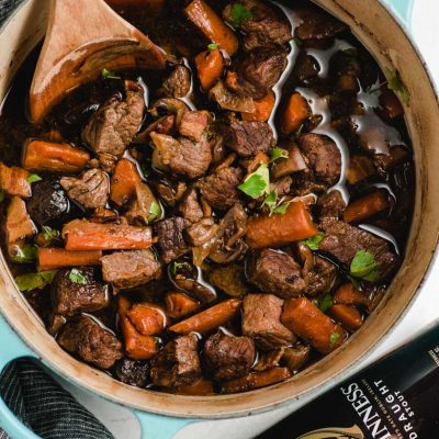 Dutch oven filled with beef stew and a wooden spoon scooping it out.