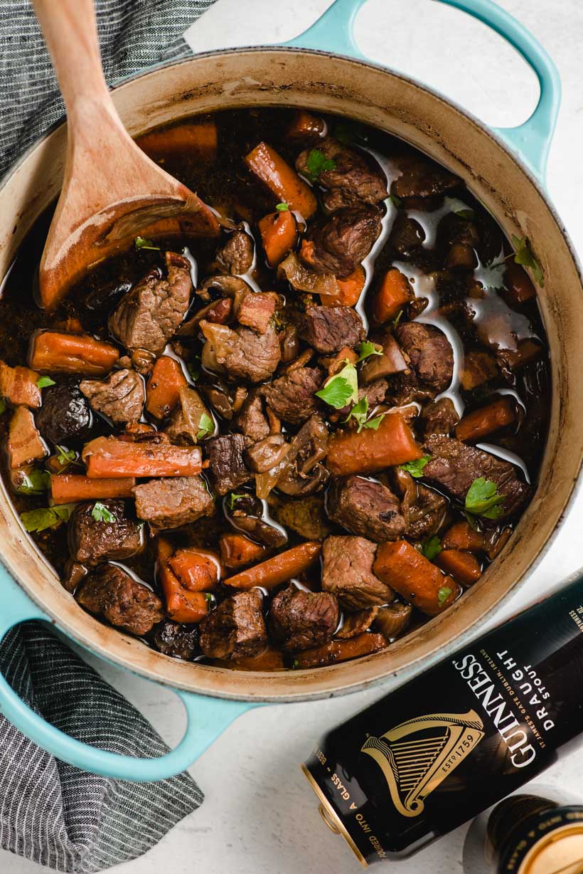 Dutch oven filled with beef stew and a wooden spoon scooping it out.