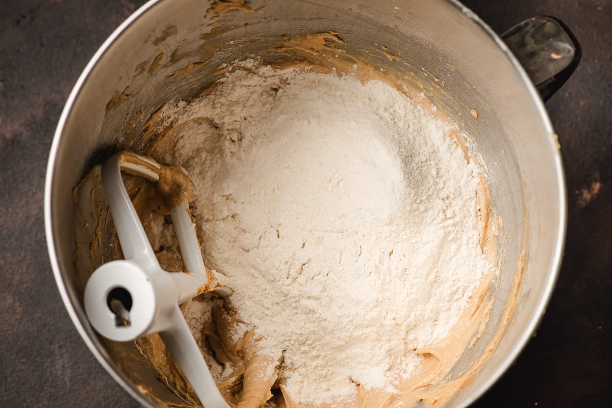 Flour mixture dumped on top of peanut butter cookie dough in the bowl of an electric mixer.