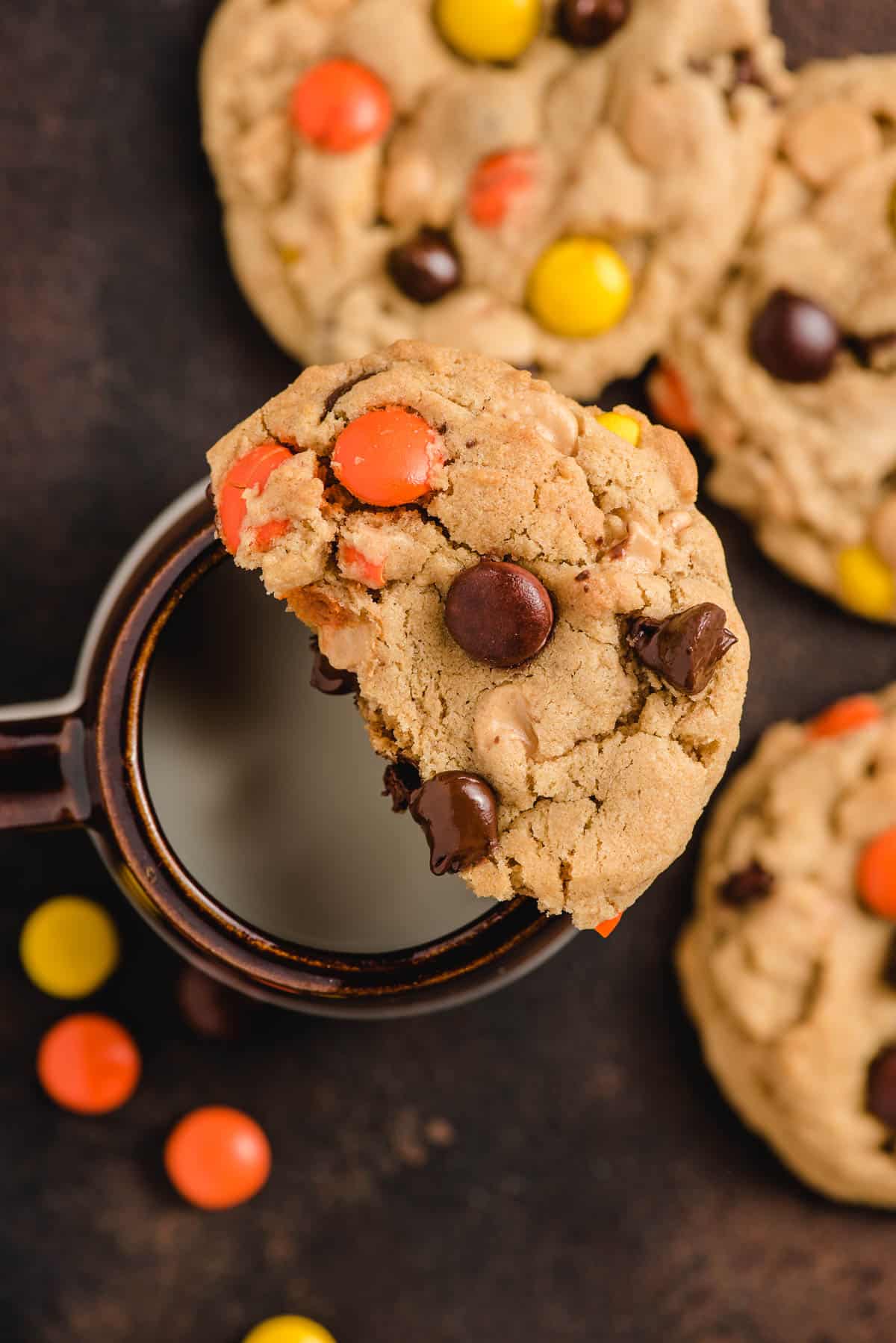 Half of a peanut butter and chocolate chip cookie sitting on top of a mug of milk.