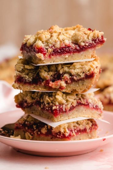 Stack of oatmeal pecan raspberry bars on a pink plate.