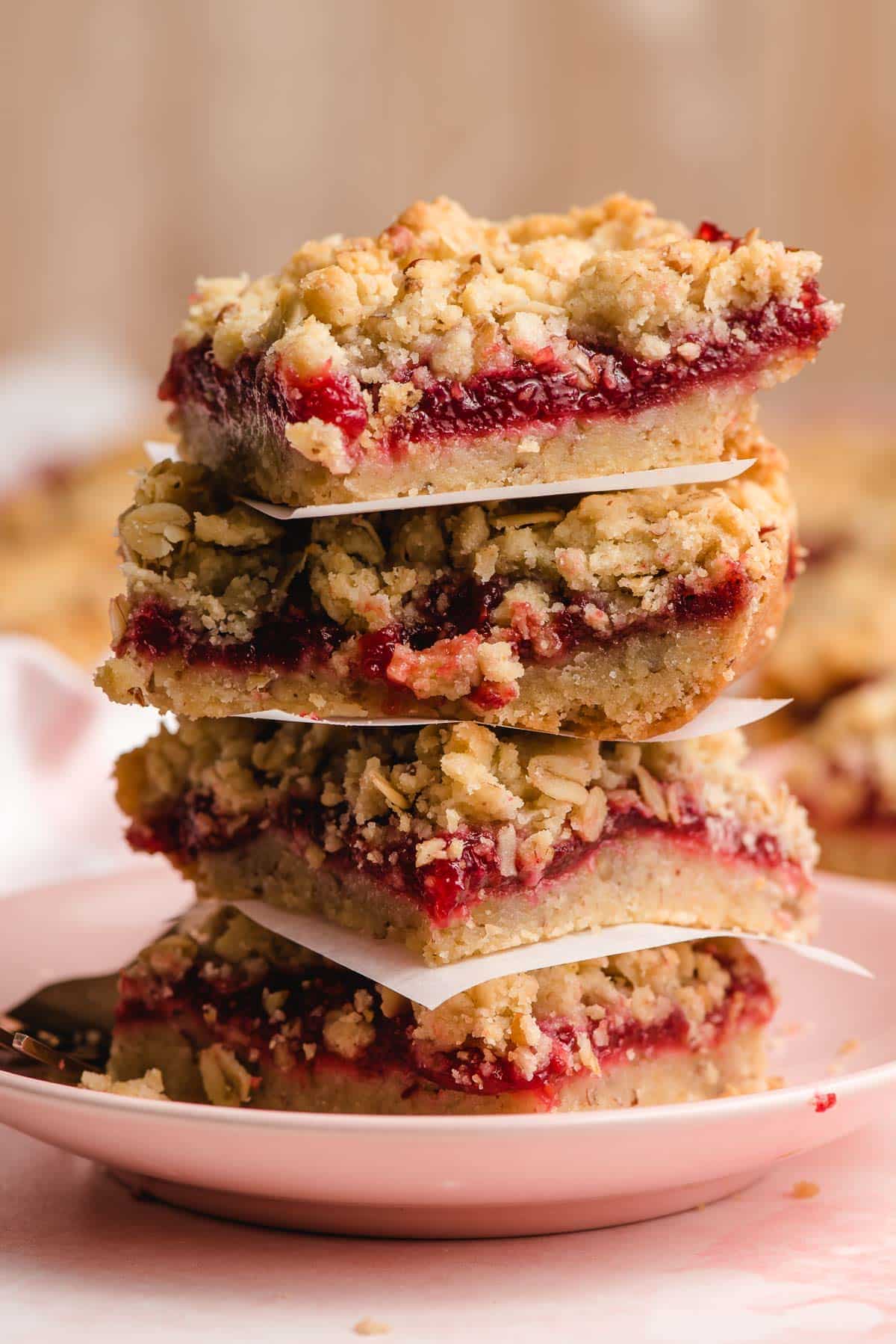 Stack of oatmeal pecan raspberry bars on a pink plate.