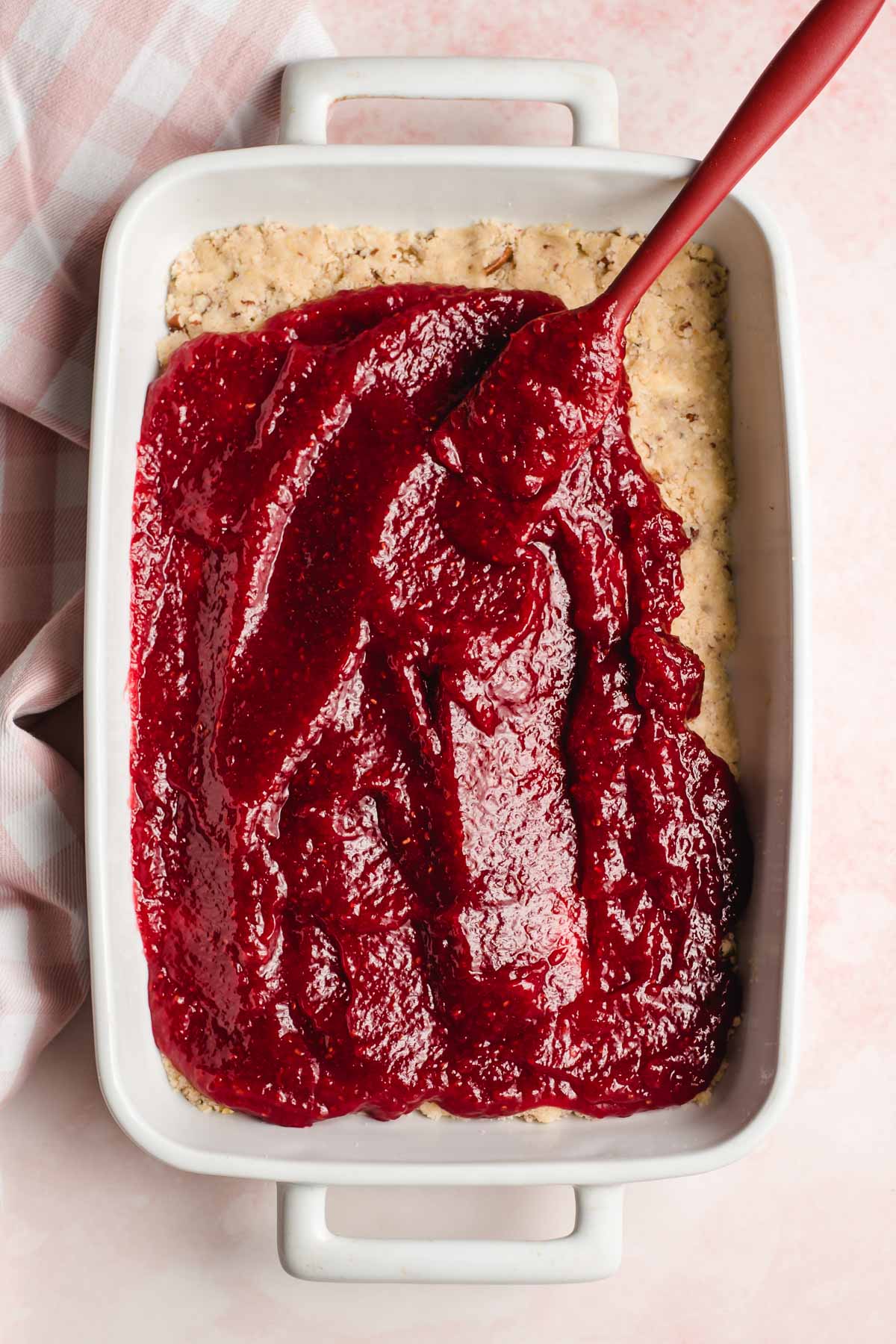 Raspberry jam being spread over a shortbread crust.