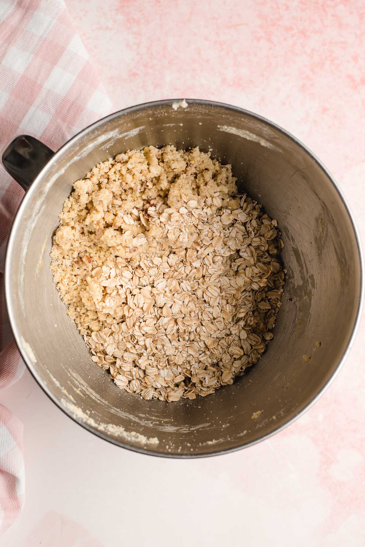 Oats and a butter, flour, sugar, and egg mixture shown in the bowl of an electric mixer.