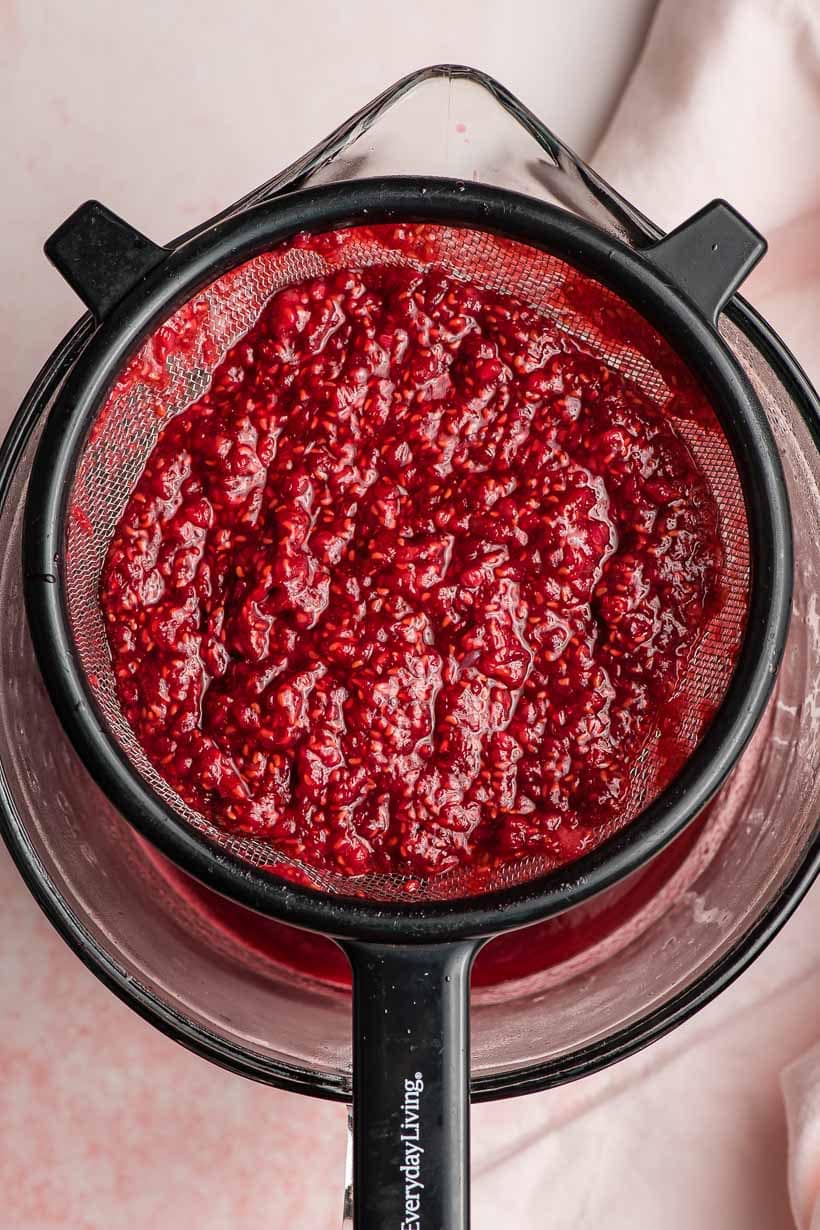 raspberry syrup being strained through a strainer