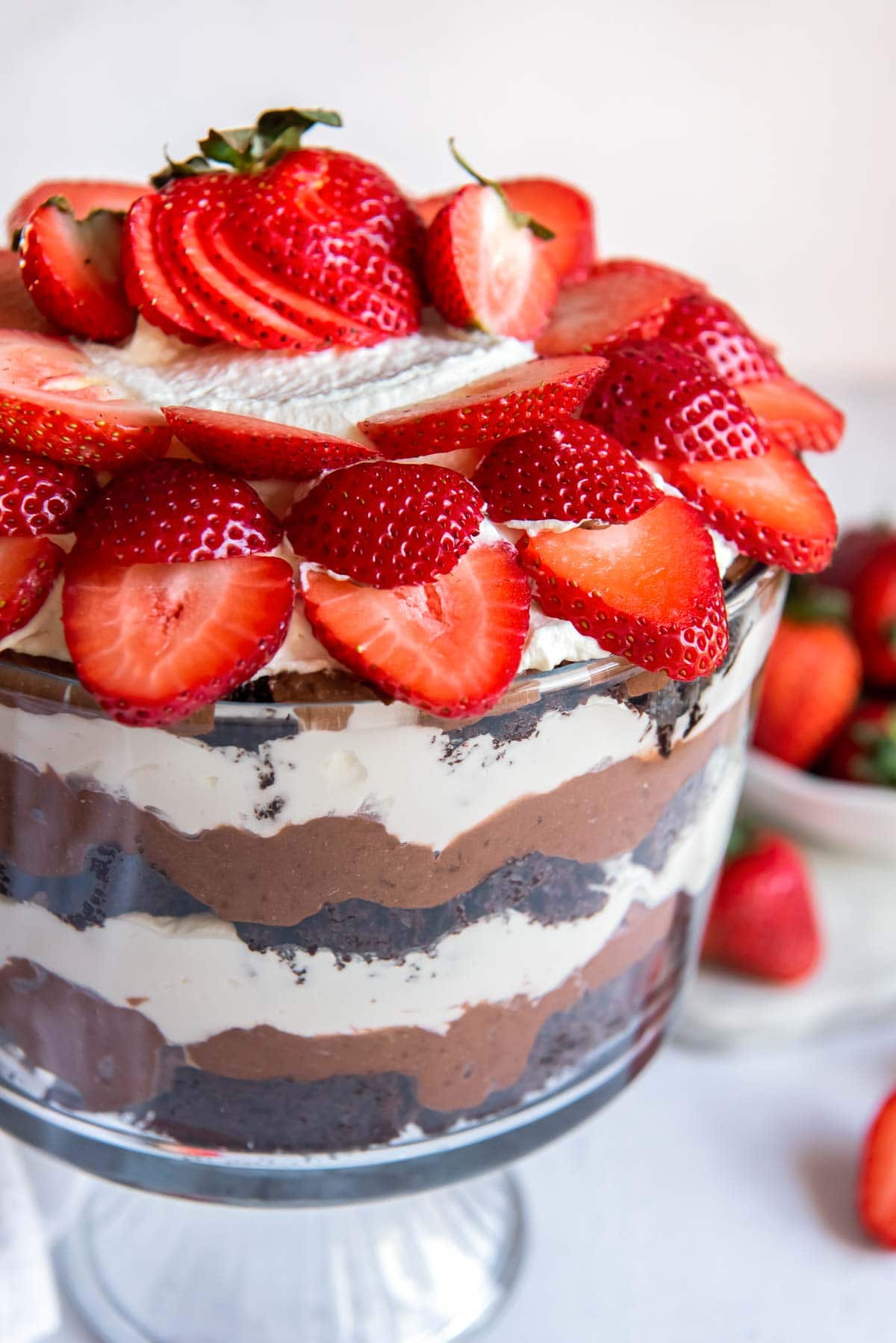 Layers of chocolate cake, chocolate pudding, and whipped cream shown in a trifle bowl and topped with sliced strawberries.