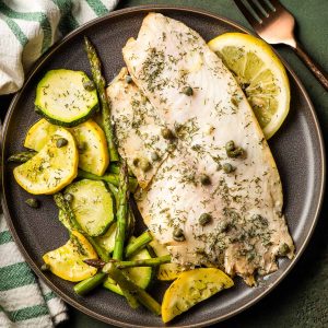 Grilled tilapia on a plate with sliced squash, zucchini, and asparagus.