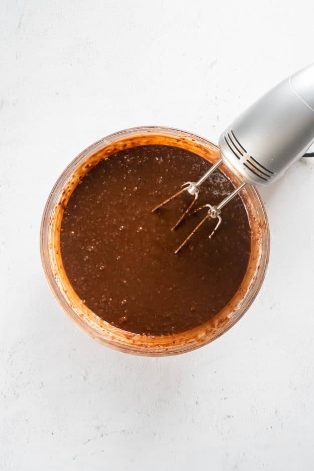Chocolate cake batter in a glass bowl with a hand blender next to it.