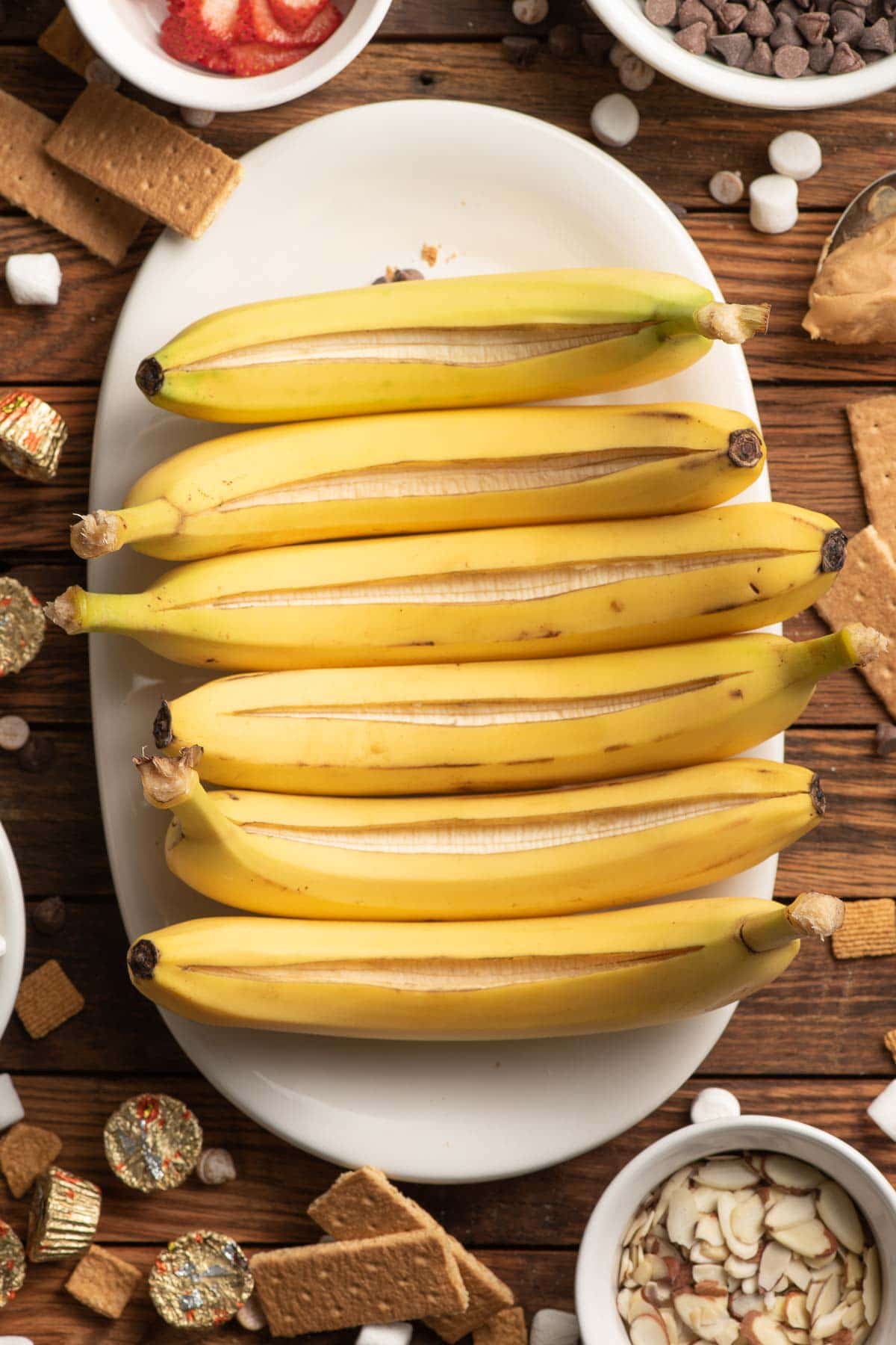 Bananas lined up on a white platter, with each one sliced down the middle.